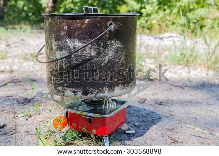 Small camping gas stove and  large blackened pot closeup on nature