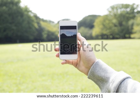 Hand of a woman taking a picture of the park in the smart phone