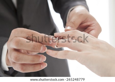 Close up on hand of a man put on an engagement ring on the finger of the bride