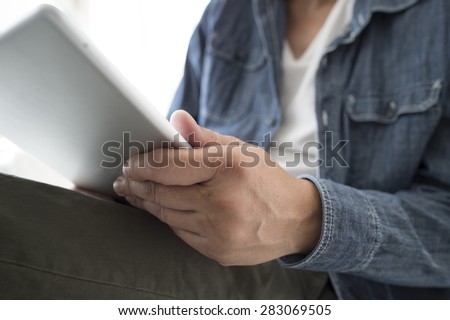 Side view of a casual smiling young Afro man using digital tablet on sofa