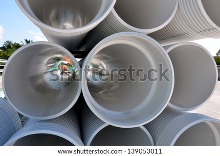 A Unique Perspective Of A Stack Of White Industrial PVC Sewer Pipes With Construction Site Visible Through Pipes