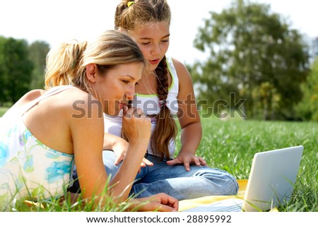 Funny mom and daughter with modern laptop outdoors