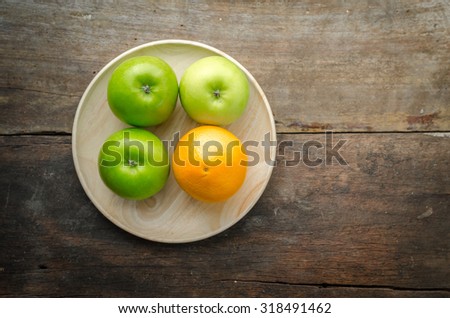 Green apples and orange on wooden plate, fresh fruits on wooden disk
