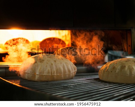 Flatbreads. fresh pita taken from oven. Quboos Arabic Bread making process the dough cut in to round shape passing through the conveyor belt. Fresh round pita is taken from the oven. bread of factory 
