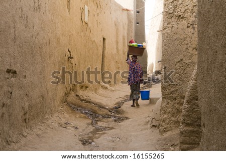 Woman carrying basket on head in narrow street
