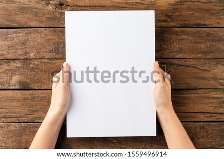 Overhead shot of woman’s hands holding blank paper sheet on rustic wooden table. Close up 商業照片 © 