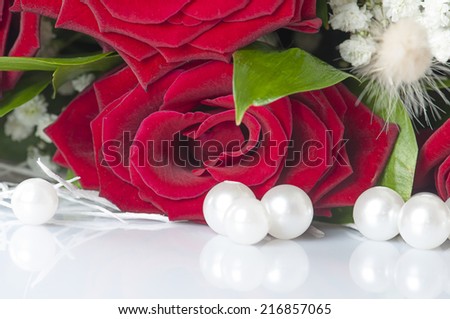 red roses and white mother-of-pearl pearls are reflected on white background