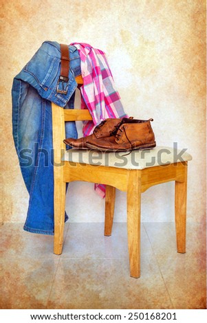 still life with plaid shirt, jeans and boots on wooden chair over grunge background