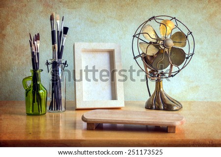 White photo frame, antique fan and paintbrush in the glass bottles on wooden table over grunge background