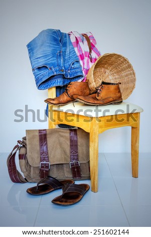 still life with plaid shirt, boots, and jeans on wooden chair over grunge background, casual vintage style.