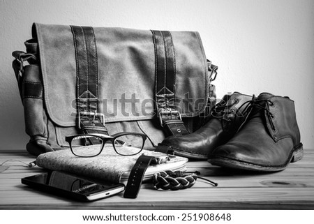 Still life with casual man, boots and bag on wooden table over grunge background, black and white