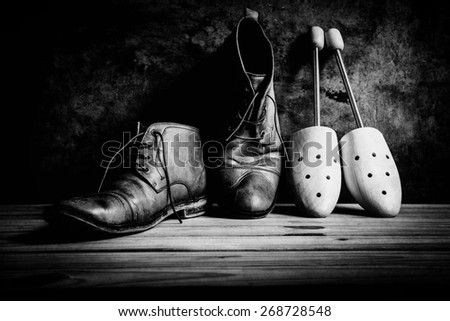 Still life with boots and wooden shoe tree on wooden table over grunge background, black and white
