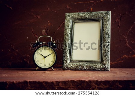 Still life with black vintage clock and photo frames on brown stone table over stone grunge background.