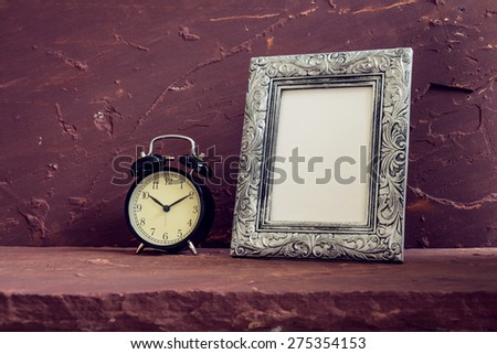 Still life with black vintage clock and photo frames on brown stone table over stone grunge background.