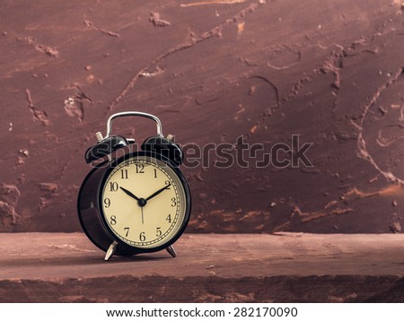 Still life with black vintage clock on brown stone table over stone grunge background