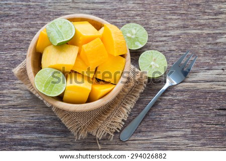 Slice of mango and green lemon in bowl on wooden background