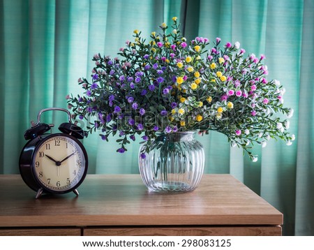Bouquet of flowers with vintage clock on a wooden table over green curtain background in the bedroom