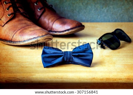 Men's casual, bow tie with sunglasses and boots on wooden over wall grunge background