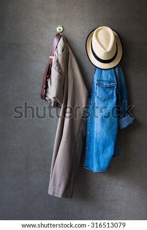 Men\'s casual outfits, brown hat, brown pants and jeans shirt hanging over gray grunge background