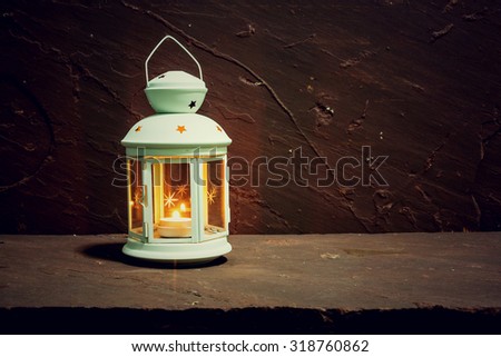 Christmas decoration lantern and candle on brown stone table over stone grunge background, rustic style