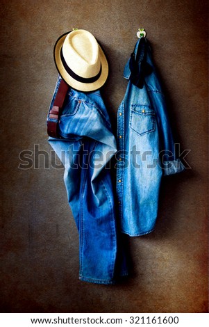 Men\'s casual outfits, blue jeans, jeans shirt, brown hat and bow tie hanging over gray grunge background