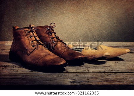 Men\'s boots and wooden shoe tree on wooden table over wall grunge background