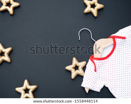 Baby shower concept with winter or Christmas theme. A white and red baby bodysuit on a dark background with golden stars. Baptism invitation. New baby birth announcement. Top view. Zdjęcia stock © 