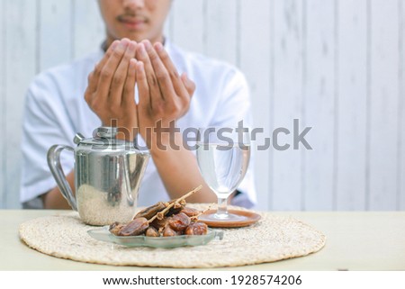 Iftar dish with muslim man hand praying to Allah. Dates fruit with glass of mineral water and teapot on the table. Traditional Ramadan, iftar meal. Ramadan kareem fasting month concept.