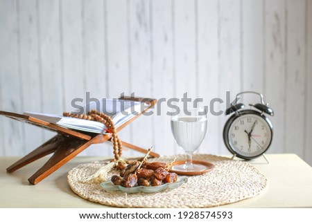 Kurma or dates fruit with glass of mineral water, holy book Al-Quran, alarm clock and prayer beads on the table. Traditional Ramadan, iftar meal. Ramadan kareem fasting month concept