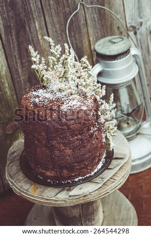 Homemade Chocolate Cake with Coconut Flakes and Dried Flower Decoration on a Small Vintage Wood Reel. Retro Lantern Included. Rusty Iron Floor and Moldy Wood Background