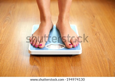Female bare feet with weight scale on wooden floor