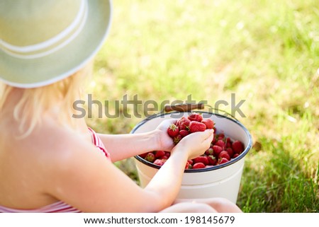 Closeup view of a young woman sitting next to a bucket full of fresh strawberries