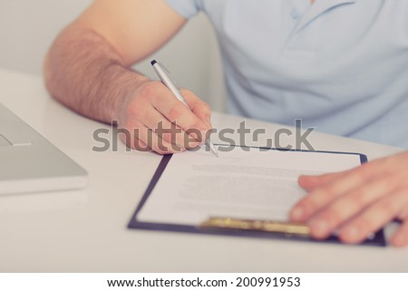 Young businessman in blue polo shirt signs a contract on white table, toned