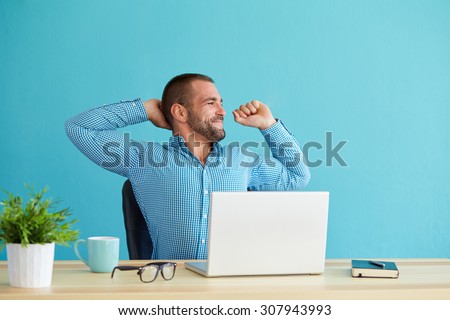 Man working at desk in office stretching his back at desk
