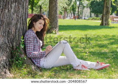 The girl draws sketches on paper sitting on the grass in the park