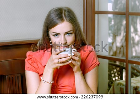Girl with blue eyes dressed in red blouse drinking coffee in a restaurant