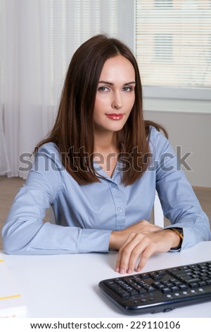 The girl sits at a table near the keyboard in the office