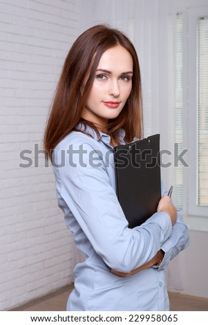 Woman in formal clothes standing holding a folder in half turn