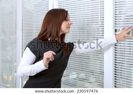 Girl in office peeking through window blinds on the street in anticipation