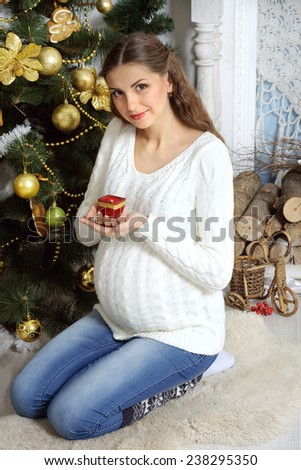 Pregnant girl in a sweater against the backdrop of Christmas trees sits on his lap and holding a candle