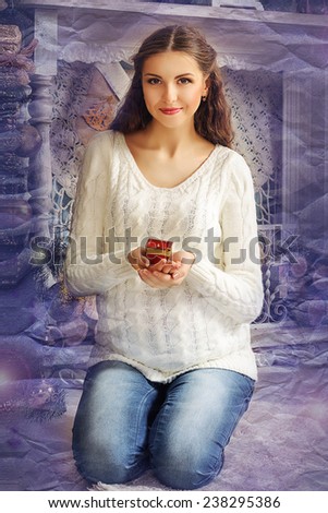 Pregnant girl in a sweater against the backdrop of the fireplace sits on his lap and holding a candle