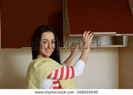 Brunette girl in home clothes opens the door cupboard. She stands dressed in blue overalls and a white T-shirt and on the shoulder of her green towel. She looks at the camera and smiling cheerfully.