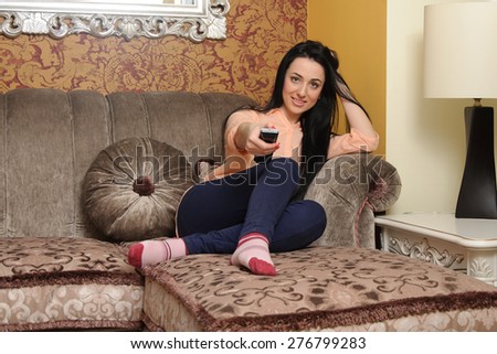 Woman in casual clothes sitting on a couch and holding a remote control for her TV
