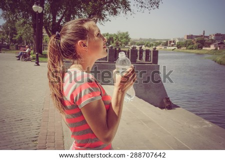 Sports woman drinks water against the embankment outdoors