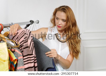 Girl chooses clothes in clothes shop against a light background