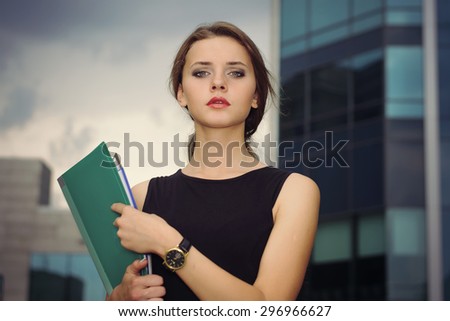 Business female in formal clothes goes on city\'s business district with folders for papers in her hands