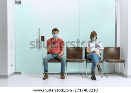 A guy and a girl in medical masks, sitting in a queue, and waiting for a doctor's appointment in the hospital. Imagine de stoc © 