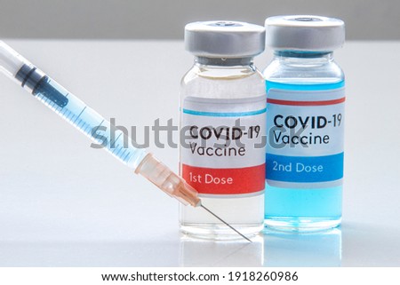 1st dosis and a 2nd dosis of covid-19 vaccine on a vial bottle and injection Syringe on a white table