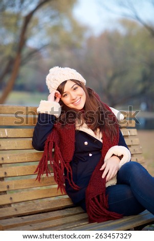 Girl sitting on bench in park in the Winter looking at camera