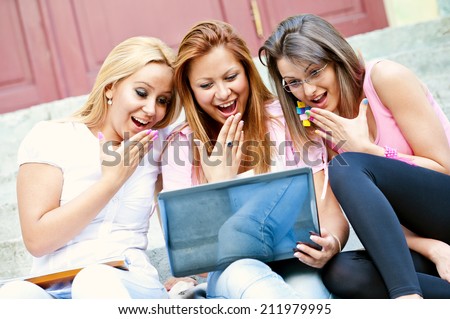 happy young high school students or college girls sitting on the steps outside the school loud laugh and a break from school with a laptop in the hands/happy young high school students